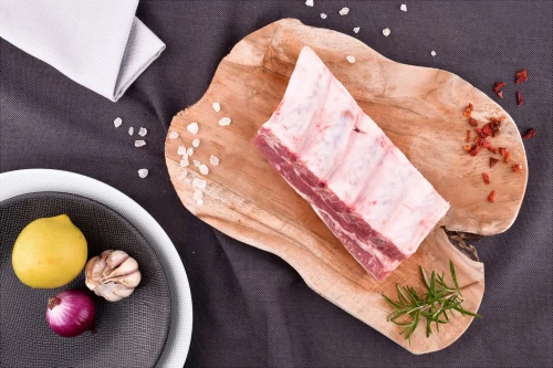 Surowe żeberka wieprzowe EKO 500g na drewnianej desce z rozmarynem, solą, chili, cytryną, czosnkiem i cebulą
