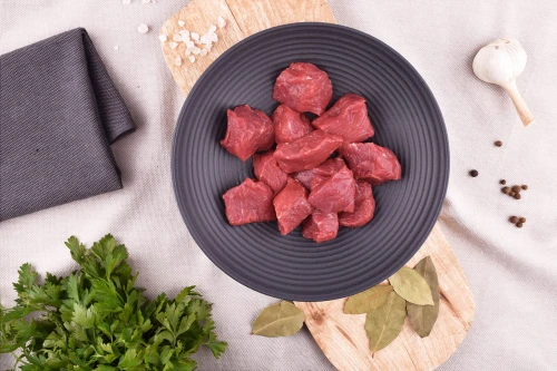 Surowe kawałki wołowiny gulaszowej EKO 400g w misce na drewnianej desce z przyprawami i pietruszką
