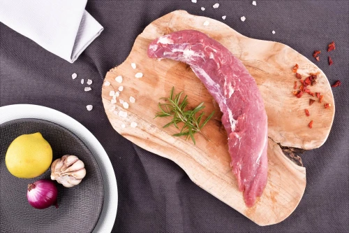 Surowa polędwica wieprzowa EKO 500g na drewnianej desce z przyprawami i cytryną